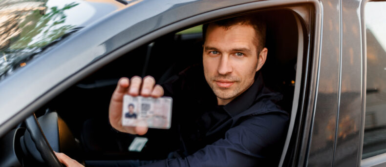 Man behind the wheel looking out window and holding up his driver's license - car insurance in Georgia