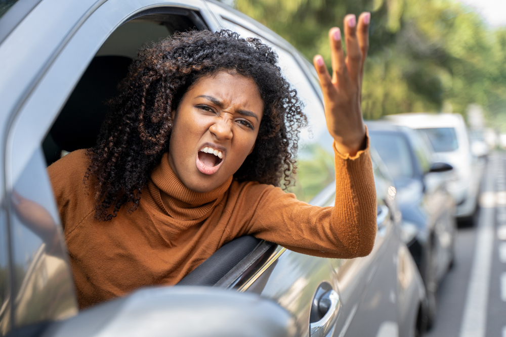 Angry young woman leans out driver's side window yelling - cheap car insurance in Georgia
