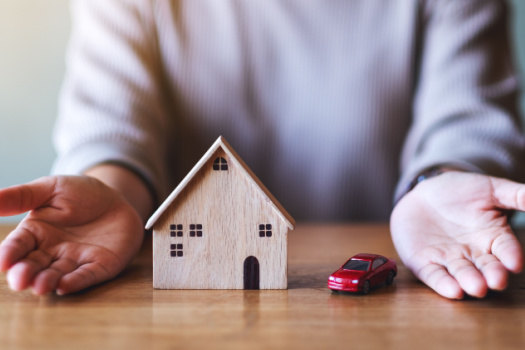 Pair of hands on table around a house and a car signifying bundling car insurance and home insurance.
