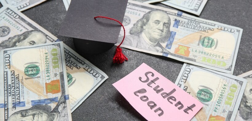 Graduation cap, U.S. dollar bills, and a note reading student loan, illustrating the financial reality of student loans in Georgia.