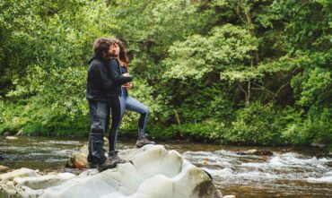 Young couple hugging by stream during hike, cheap car insurance in Georgia.