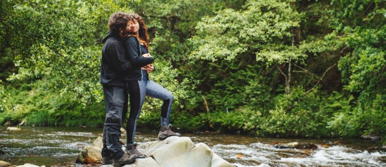 Young couple hugging by stream during hike, cheap car insurance in Georgia.