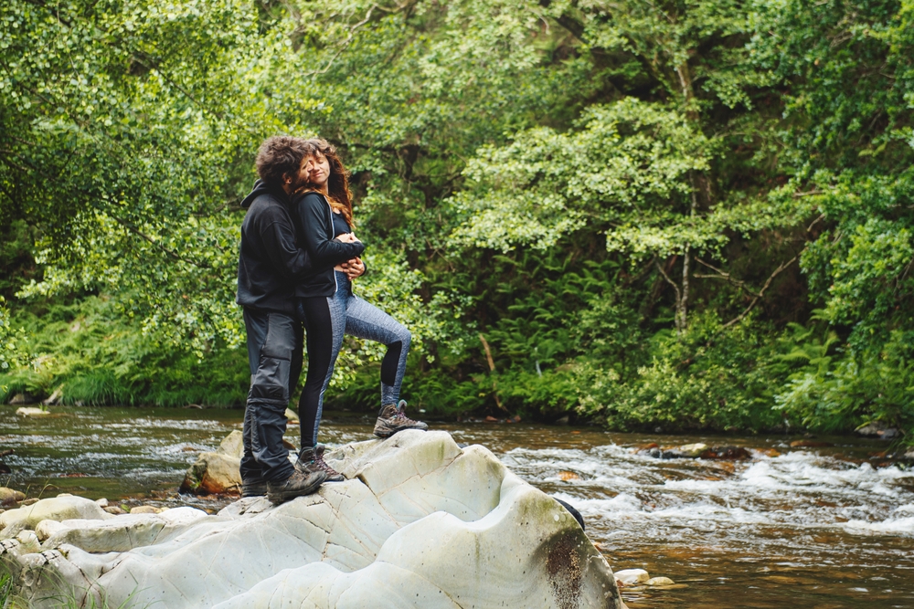 Young couple hugging by stream during hike, cheap car insurance in Georgia.