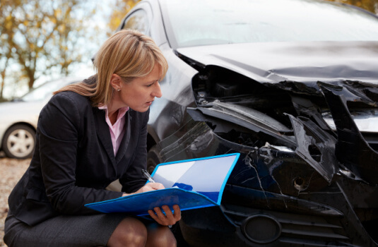 A woman insurance adjuster examines the damage done to a vehicle after a crash, cheap car insurance in Georgia.