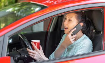 Woman driver holding a cup and a phone, distracted driving concept - cheap car insurance in Georgia.