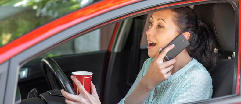 Woman driver holding a cup and a phone, distracted driving concept - cheap car insurance in Georgia.