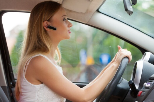 Female driving with a Bluetooth, hands-free device in her ear - cheap car insurance in Georgia.