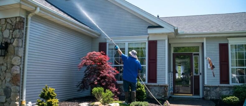 Homeowner power washes roof as part of home maintenance checklist - cheap home insurance in Georgia.