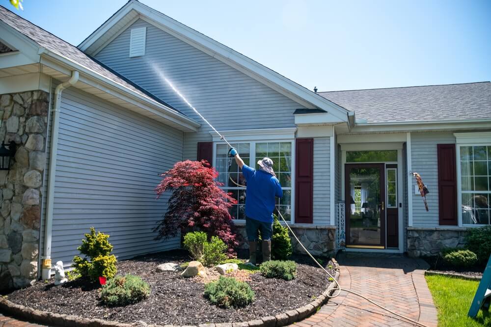 Homeowner power washes roof as part of home maintenance checklist - cheap home insurance in Georgia.