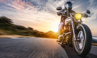 Helmeted motorcyclist rides a cruiser at speed on an open road at sunset, raising questions like buy a motorcycle without a license.