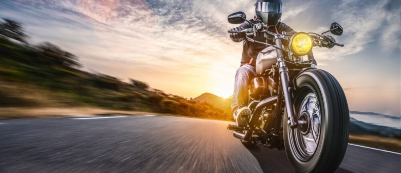Helmeted motorcyclist rides a cruiser at speed on an open road at sunset, raising questions like buy a motorcycle without a license.
