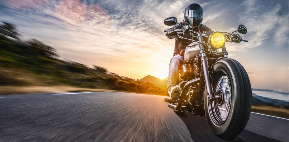 Helmeted motorcyclist rides a cruiser at speed on an open road at sunset, raising questions like buy a motorcycle without a license.