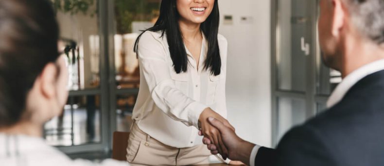 Smiling woman shaking hands during a meeting with insurance agents, with paperwork on the table — representing ways of reducing renters insurance premium costs through good policies, discounts, and smart financial planning.