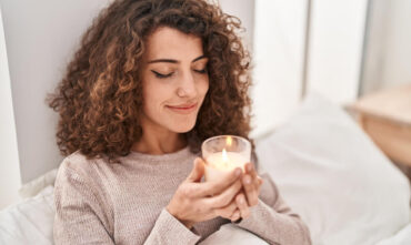 Woman smelling a scented candle in her home - Southern Harvest Cheap homeowners in Georgia.