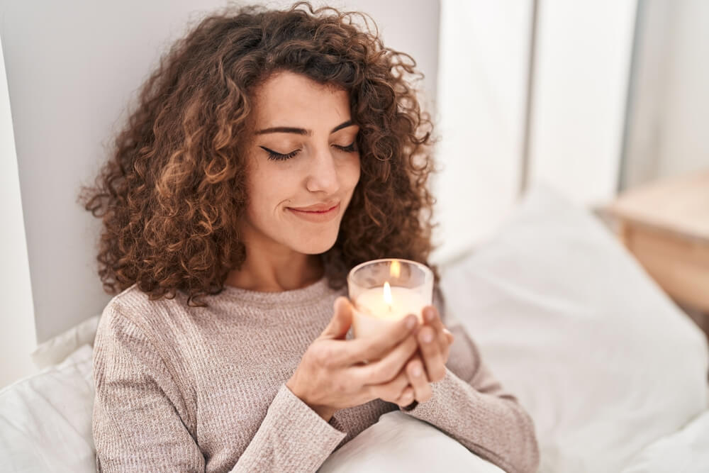 Woman smelling a scented candle in her home - Southern Harvest Cheap homeowners in Georgia.