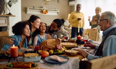 Happy multiracial parents and their kids laughing during family meal on Thanksgiving in dining room.