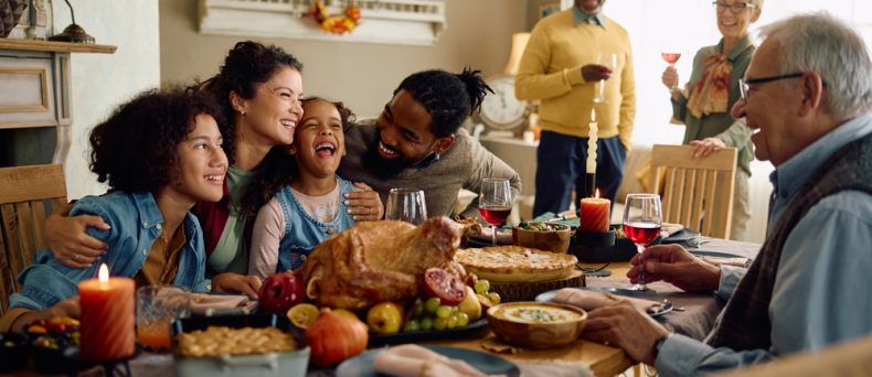 Happy multiracial parents and their kids laughing during family meal on Thanksgiving in dining room.