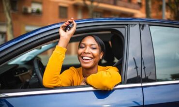 Happy woman leans out the window of her new car dangling her car keys - cheap car insurance in Georgia.