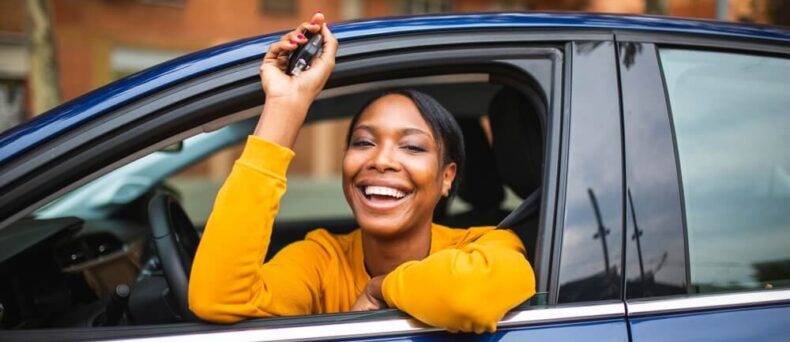 Happy woman leans out the window of her new car dangling her car keys - cheap car insurance in Georgia.