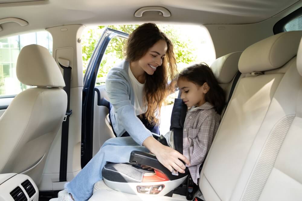 Mother buckling in her daughter in her car seat happy that she purchased the safest car of 2026.