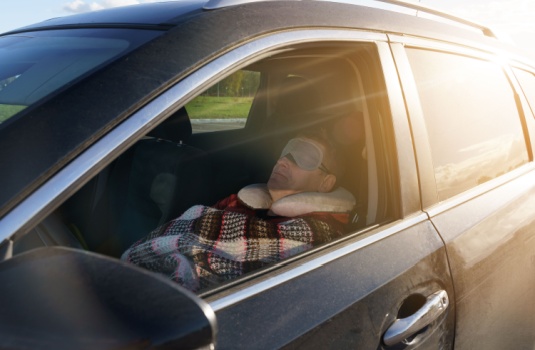 Man sleeps in the front seat of his car.
