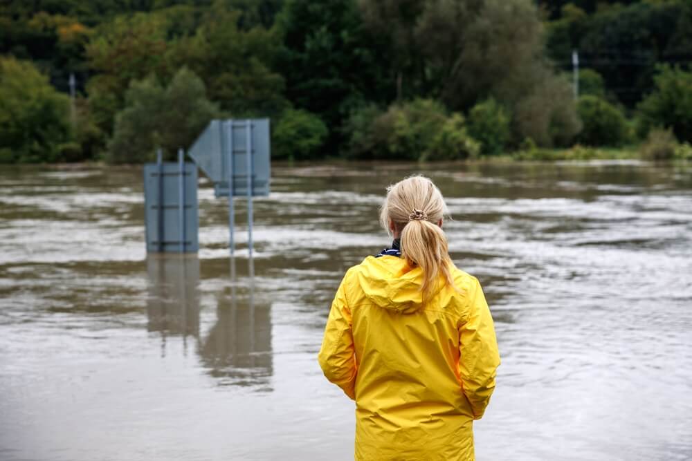 Flooded river. Worried woman looking at overflowing water during flood. Extreme weather and natural disaster - cheap home insurance in Georgia.