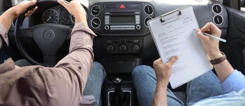 Defensive driving course in-car training session with a student driving while an instructor takes notes on a clipboard during a road skills evaluation.