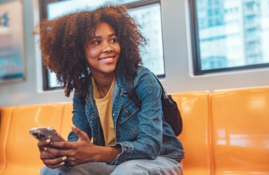 Young woman smiling, sits in railcar as she commutes to work.