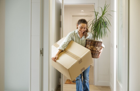 Woman arriving at her new rental house with her plant and a box with her belongings with renters insurance in Georgia to protect her belongings.