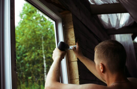 A worker specializing in renovating older homes works on a window, home insurance for historic homes.