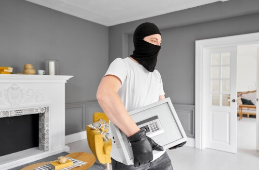 Thief with black mask stealing modern metal safe with an electronic lock, concept of renters insurance theft coverage. 