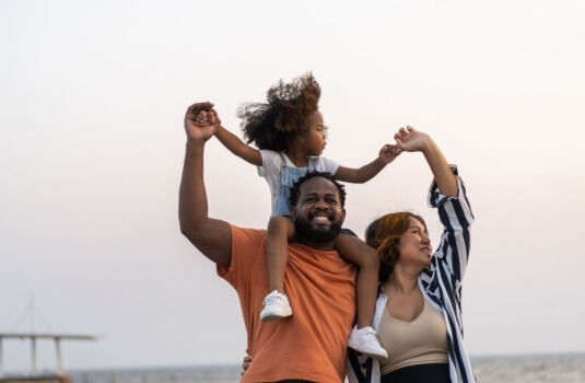 African American family of father, mother, and daughter holding hands and smiling for having taken advantage of the open enrollment for life insurance.