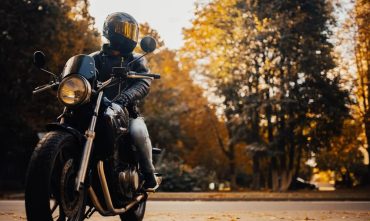 Aquí tienes la traducción al inglés: Motorcyclist with helmet and suit riding on a road protected by motorcycle safety for beginners.