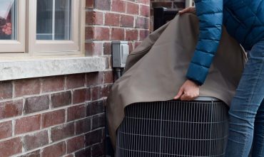 Woman putting cover on air conditioner unit outside the house during home fall maintenance checklist.