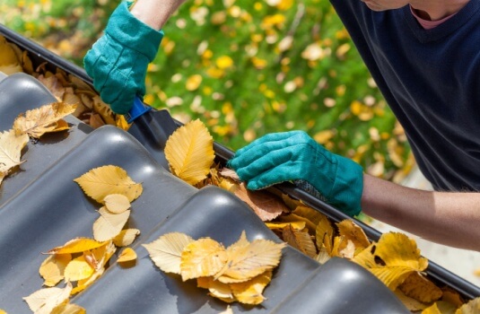 Man cleaning the gutter from autumn leaves during a fall home maintenance checkup.