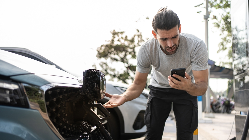 Young man outside car. EV roadside assistance needed for broken car charger problem. Helpless user need help and assistance. Electric car accident. Electric vehicle car trouble.