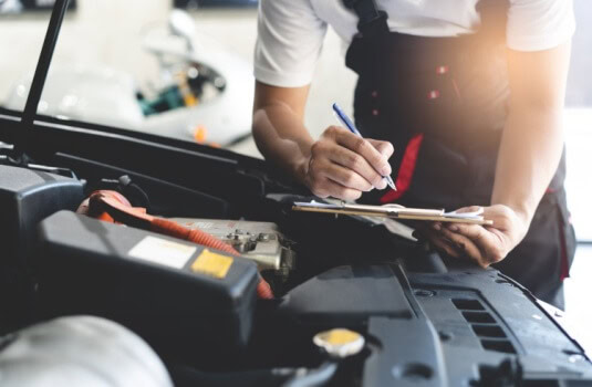 Auto check up and car service shop concept. Mechanic writing job checklist to clipboard to estimate repair quotation to client at workshop garage.