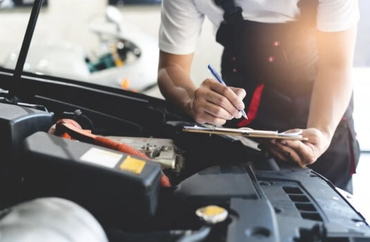 Auto check up and car service shop concept. Mechanic writing job checklist to clipboard to estimate repair quotation to client at workshop garage.