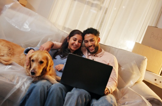 Couple sitting on couch after purchasing a home doing their after closing move-in checklist.
