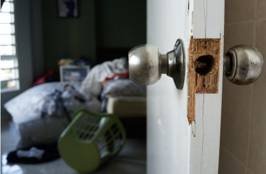 A close-up of a broken wooden door frame and a mangled door handle after a break-in, highlighting a scenario where a claim might be filed against renters policy deductibles.