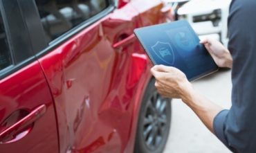 Person inspecting damage on a red car with a tablet, representing how no down payment car insurance can help cover accident costs quickly.