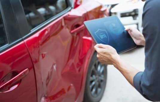 Person inspecting damage on a red car with a tablet, representing how no down payment car insurance can help cover accident costs quickly.