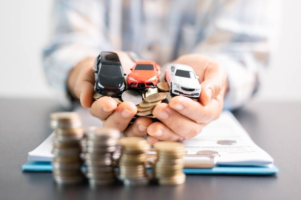 Hands holding toy cars and coins symbolizing savings, illustrating how no down payment car insurance makes coverage more affordable upfront.
