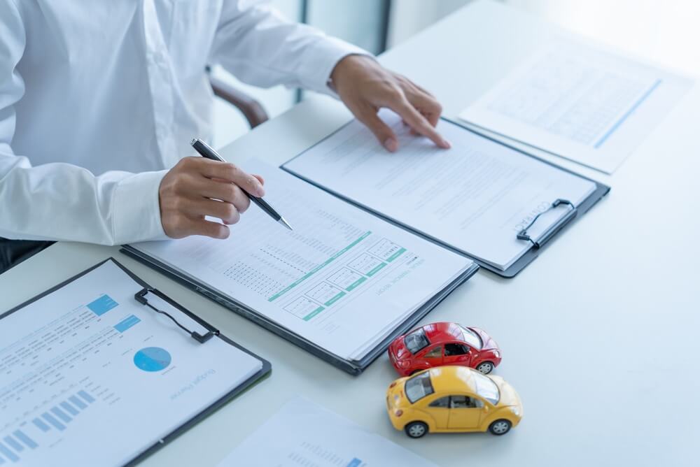 Person reviewing auto insurance paperwork with toy cars, related to checking your Georgia auto insurance status.