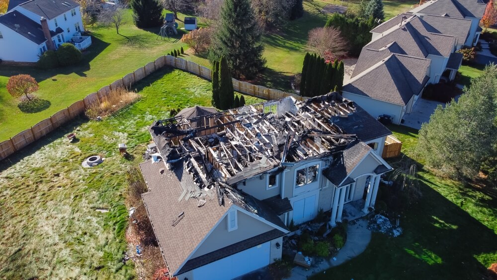 Aerial view of a severely fire-damaged suburban home with a collapsed roof and charred structure, highlighting the importance of Georgia homeowners insurance coverage for property loss and rebuilding.