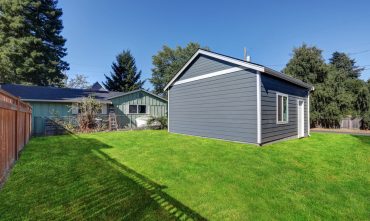 Detached gray garage with white trim located in a spacious backyard beside a single-story home, illustrating a structure that may be covered under homeowners insurance.