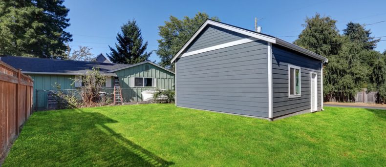 Detached gray garage with white trim located in a spacious backyard beside a single-story home, illustrating a structure that may be covered under homeowners insurance.