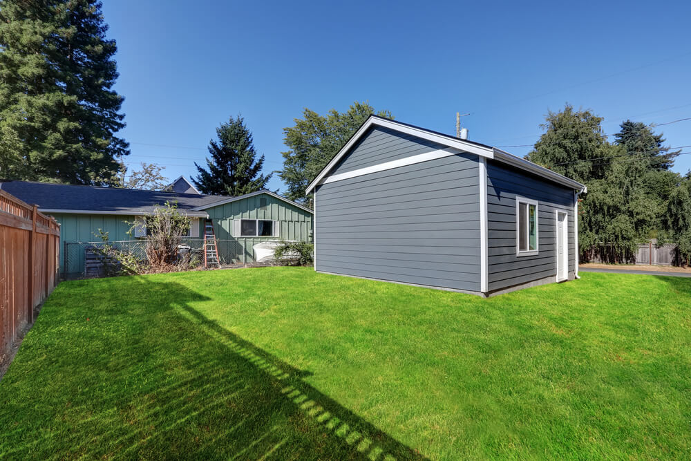 Detached gray garage with white trim located in a spacious backyard beside a single-story home, illustrating a structure that may be covered under homeowners insurance.