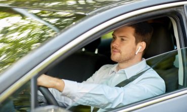 Man driving a car while wearing a wireless earpiece, illustrating hands-free driving laws that allow drivers to use voice-activated or hands-free technology while keeping their hands on the wheel.