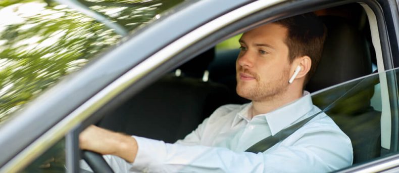 Man driving a car while wearing a wireless earpiece, illustrating hands-free driving laws that allow drivers to use voice-activated or hands-free technology while keeping their hands on the wheel.